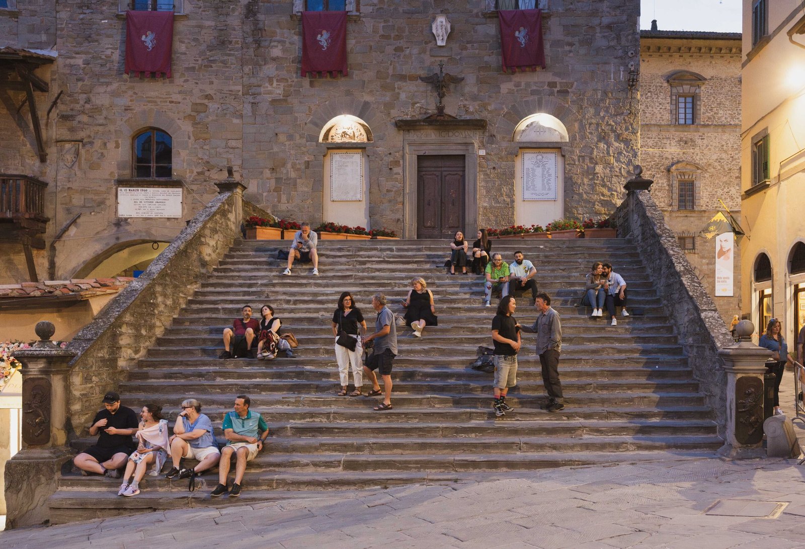 People sitting on the steps of a medieval town hall in a Tuscan piazza