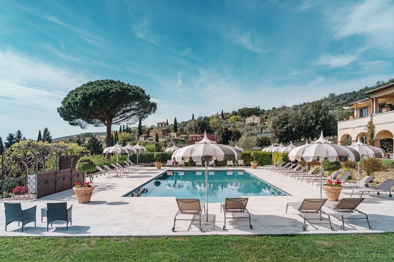 il Falconiere Piscina con lettini e ombrelloni nel giardino di una villa toscana circondata da pini marittimi