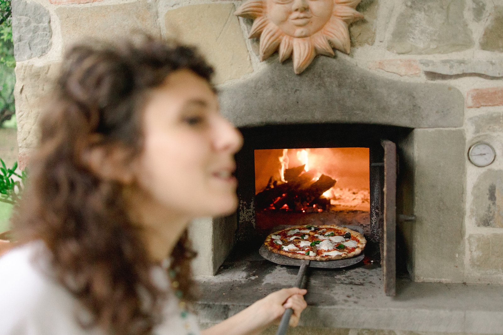 Woman sliding a pizza out of a wood-fired oven at a Tuscan villa