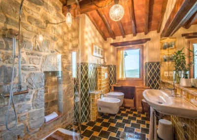 Rustic bathroom with exposed stone walls, beamed ceiling, shower and window at Villa Erbolino