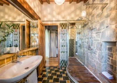 Bathroom with exposed stone wall, glass walk-in shower and colourful tiles at Villa Erbolino