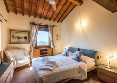 Cosy double bedroom with beamed ceiling, armchair and window onto the Chianti countryside at Villa Erbolino