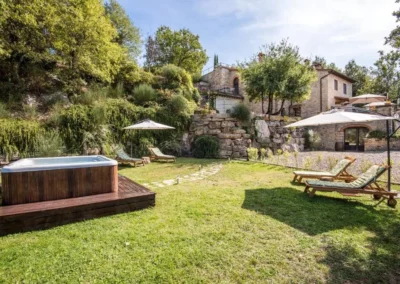Large garden lawn with hot tub, sun loungers and parasols beside the stone villa at Villa Erbolino, Chianti