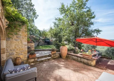 Stone garden patio with outdoor dining table, red parasol and old trees at Villa Erbolino in Chianti