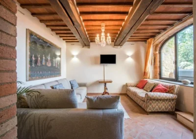 Bright living room with wooden-beam ceiling, chandelier, sofas and terracotta floor at Villa Erbolino in Chianti