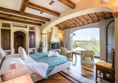 Spacious double bedroom with fireplace, armchairs and large window with countryside view at Villa Erbolino