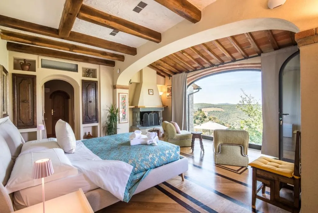villa-erbolino-chianti-master-bedroom-fireplace-view Spacious double bedroom with fireplace, armchairs and large window with countryside view at Villa Erbolino