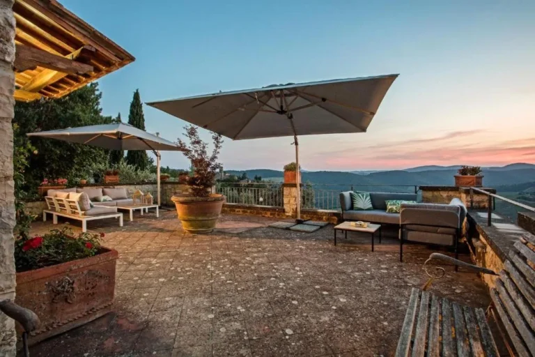 Large stone terrace with parasols, lounge seating and potted plants overlooking the Tuscan hills at Villa Erbolino Large stone terrace with parasols, lounge seating and potted plants overlooking the Tuscan hills at Villa Erbolino