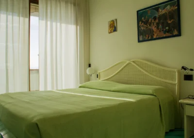 Bright double bedroom with green bedspread and long white curtains at Villa Monte Bianco