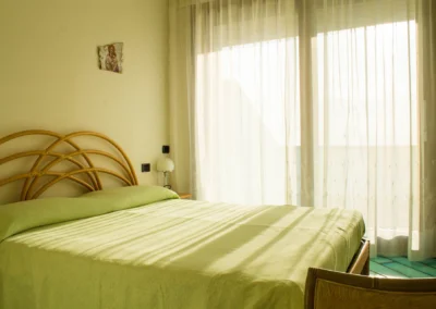 Double bedroom with a rattan headboard and sunlit curtains at Villa Monte Bianco