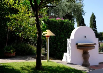 White stone fountain on the garden path among trees and cypresses