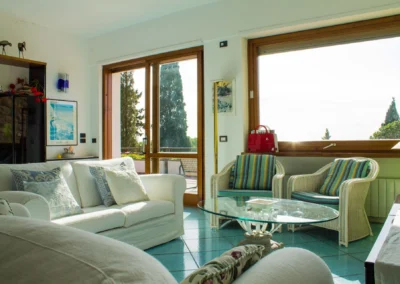 Bright living room with white sofas, wicker armchairs and large windows onto the garden