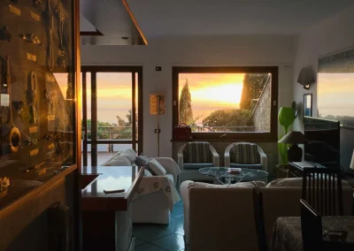 Living room of Villa Monte Bianco glowing at sunset, with sofas and a window onto the sea
