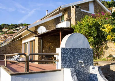 White and mosaic outdoor shower on the terrace, with the stone villa and bougainvillea behind