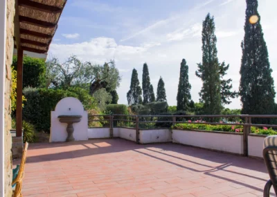 Large terracotta terrace of Villa Monte Bianco with a stone fountain, cypresses and olive trees