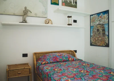 Single bedroom with a rattan bed, colourful bedspread and paintings at Villa Monte Bianco