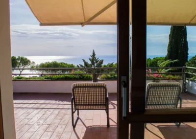 View from the living room through open glass doors onto the shaded terrace and the sea