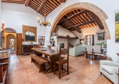 Open-plan living and dining area with brick arch, sofas, chandelier and antique furniture