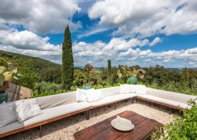 Built-in terrace lounge with white cushions overlooking cypresses and the Tuscan hills