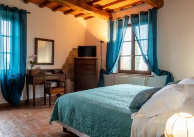 Double bedroom with desk, chest of drawers and blue curtains under a beamed ceiling