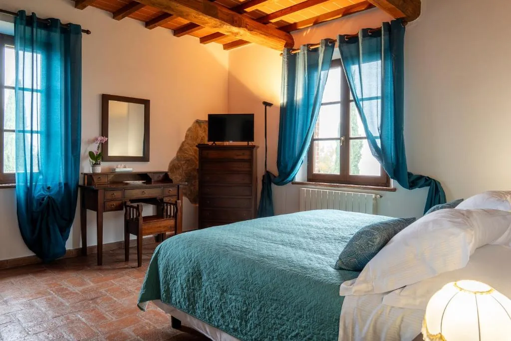 villa-tiberini-torrita-di-siena-double-bedroom-desk-window Double bedroom with desk, chest of drawers and blue curtains under a beamed ceiling