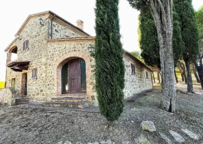 Stone cottage with arched door between cypresses on the estate