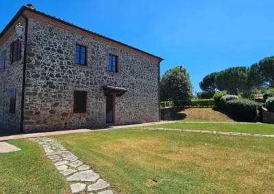 Two-storey stone farmhouse with lawn and stone path under a blue Tuscan sky