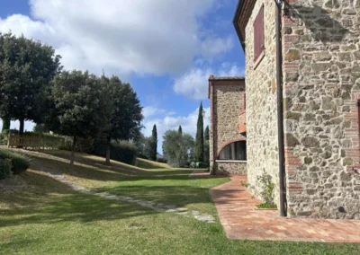Brick path and lawn along the stone walls of the villa with trees and cypresses